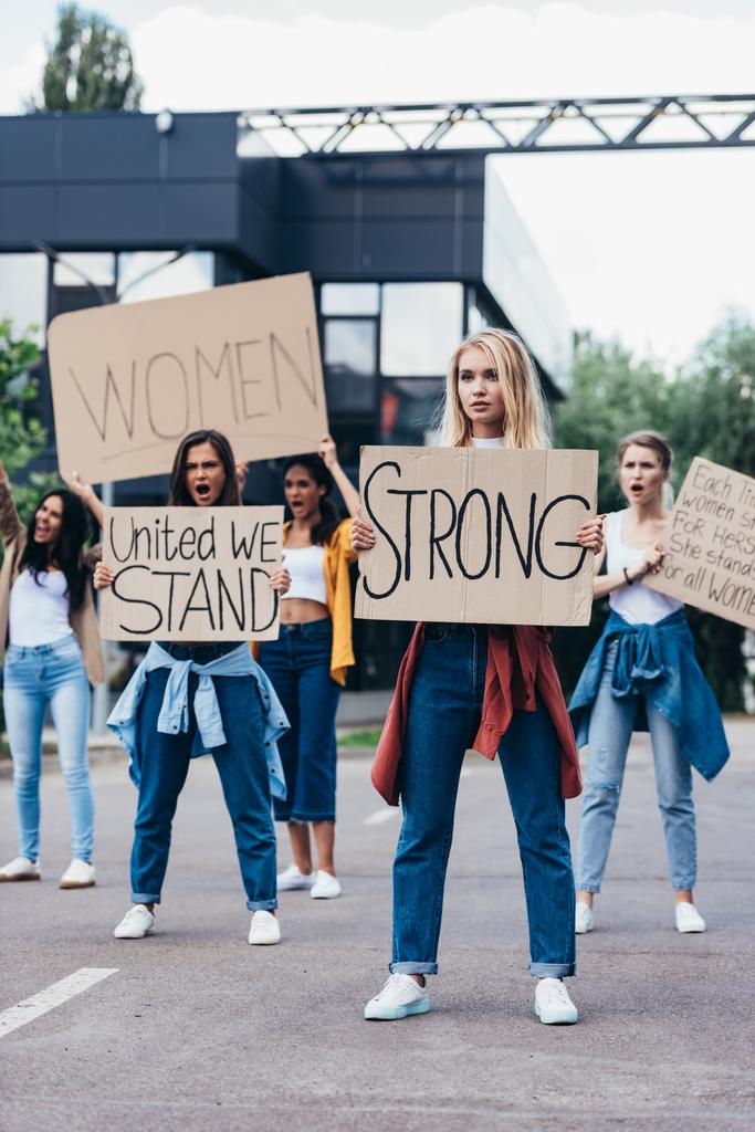 full length view of woman holding placard with word strong near feminists on street - Photo, Image