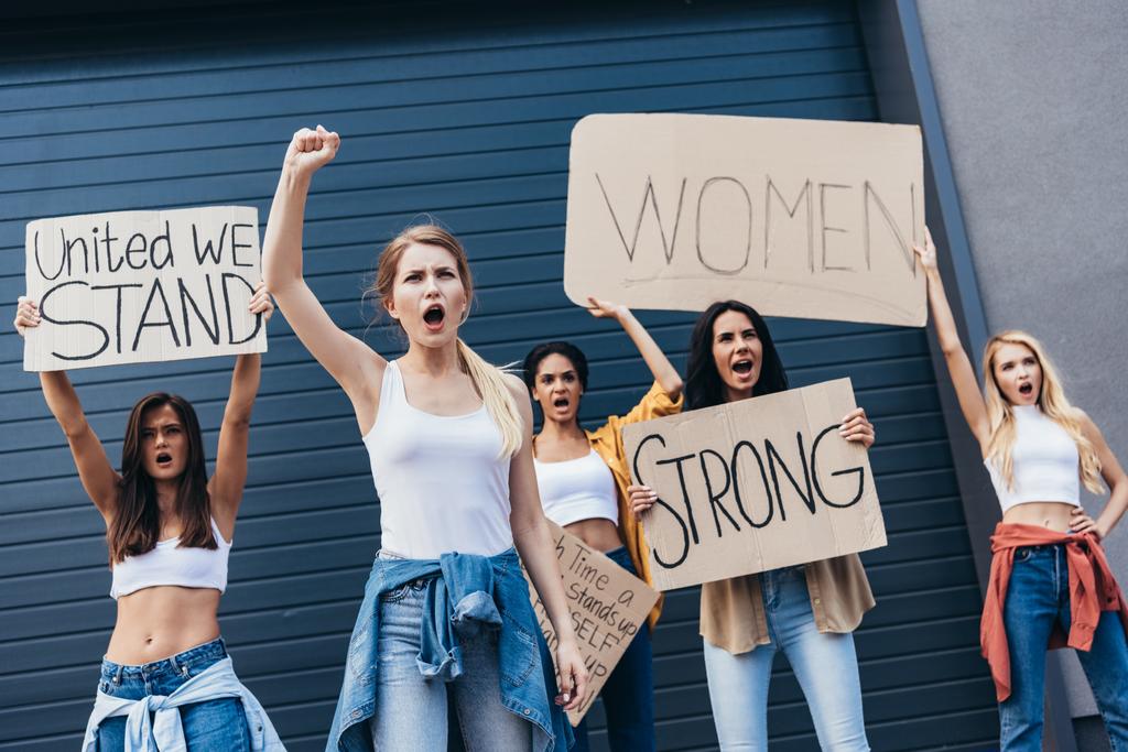 Πέντε πολυεθνικές φεμινίστριες που κρατούν πλακάτ με συνθήματα και ουρλιάζουν στο δρόμο - Φωτογραφία, εικόνα
