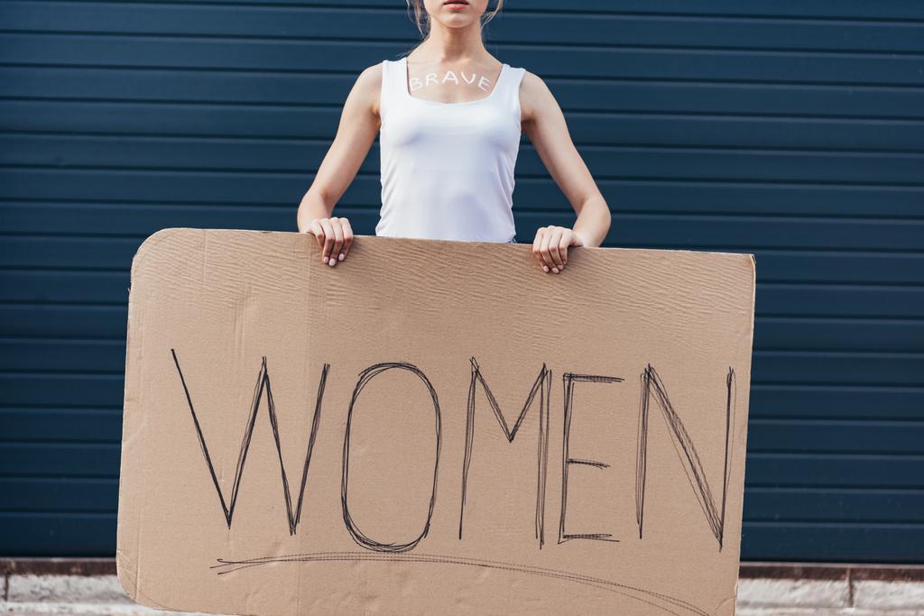 cropped view of feminist with word brave on body holding placard with inscription women on street - Photo, Image