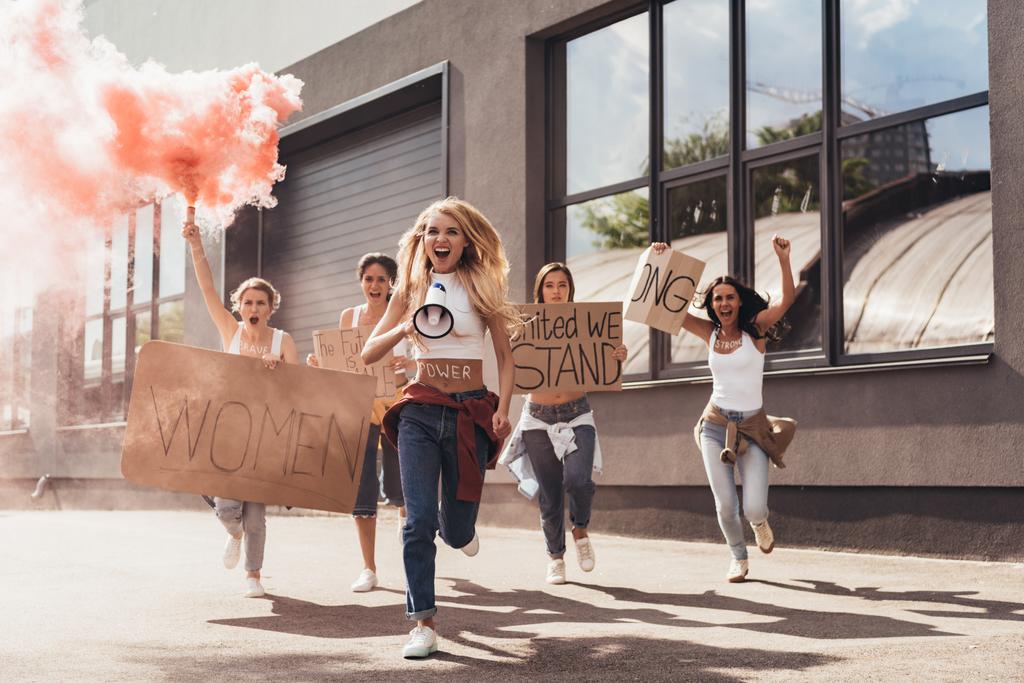 полный обзор кричащих мультиэтнических феминисток с громкоговорителем, держащих плакаты с лозунгами и бегущих по улице
 - Фото, изображение
