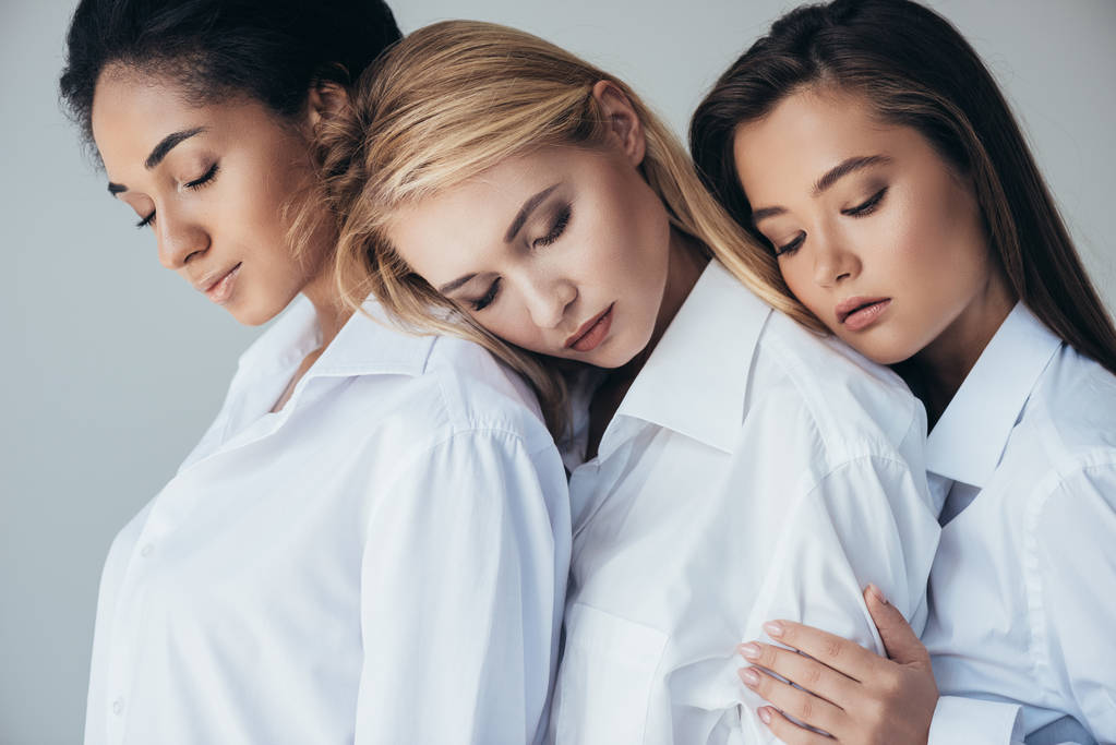 three attractive multiethnic girls in white shirts embracing isolated on grey - Photo, Image