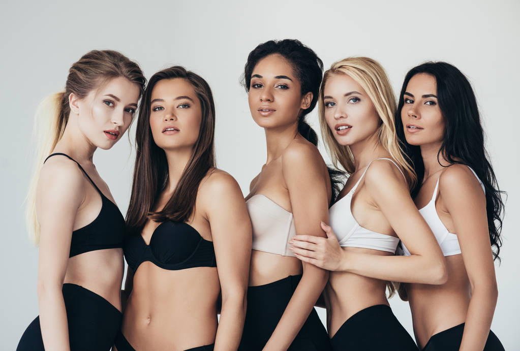 vijf sexy multi-etnische jonge vrouwen in ondergoed omarmen geïsoleerd op grijs - Foto, afbeelding