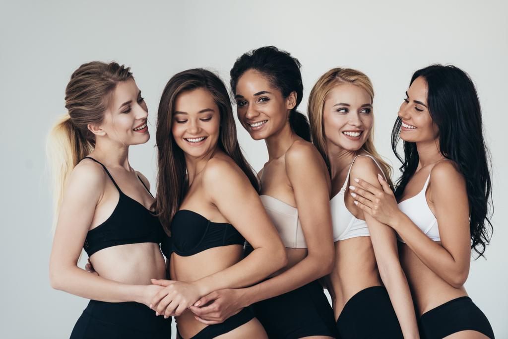 viisi seksikästä monietnistä nuorta naista alusvaatteissa syleilee ja hymyilee eristettynä harmaaseen
 - Valokuva, kuva