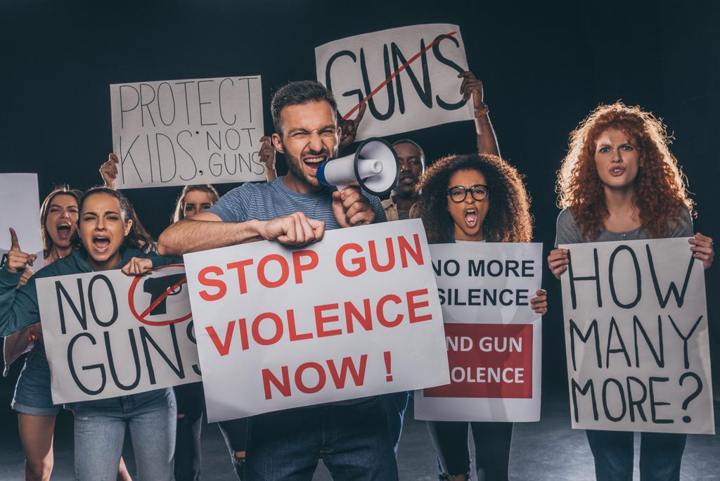 сердитий чоловік тримає плакат з насильством стоп-пістолета зараз висміює і кричить в мегафоні поблизу мультикультурних людей на чорному
  - Фото, зображення