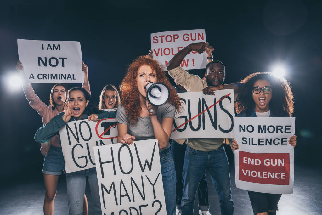 redhead girl holding placard with how many more lettering and screaming in megaphone near multicultural people on black  - Photo, Image