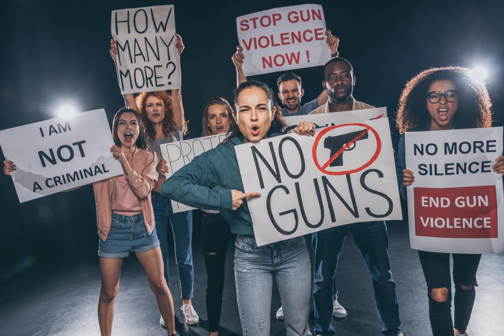 Emotionales Mädchen zeigt mit dem Finger auf Plakat ohne Waffen Schriftzug in der Nähe von multikulturellen Menschen auf schwarz  - Foto, Bild