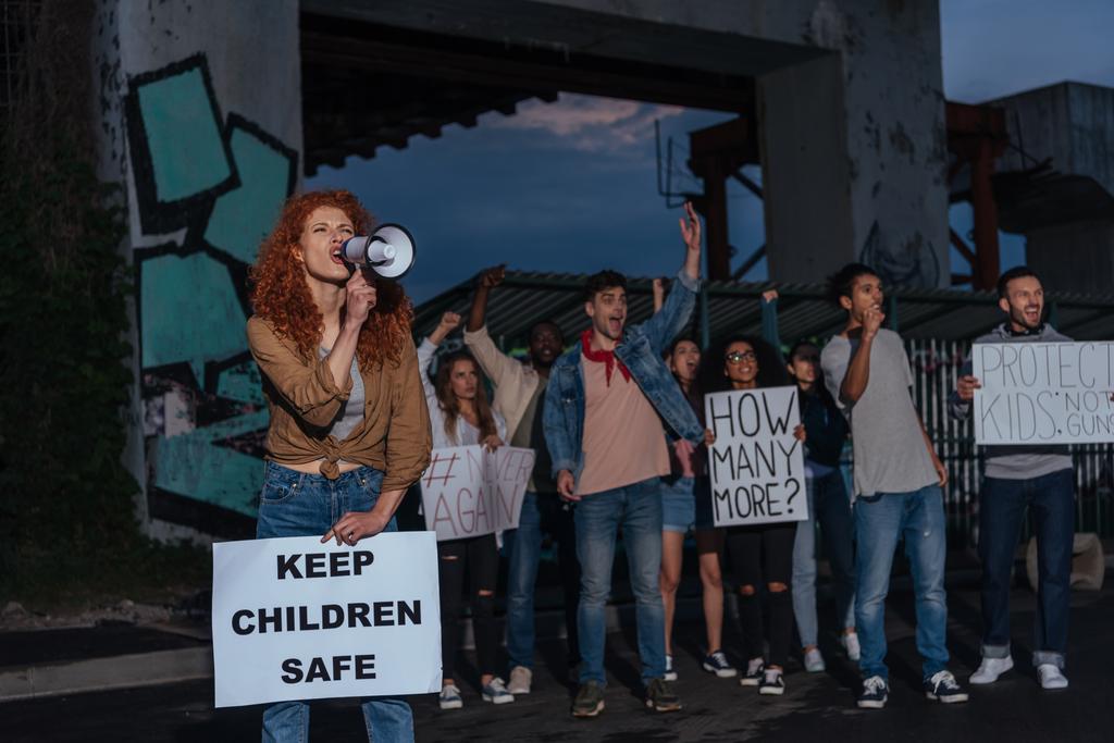 селективное внимание эмоциональной рыжей девушки, держащей плакат с безопасными надписями и кричащей рядом с мультикультурными людьми на встрече
  - Фото, изображение