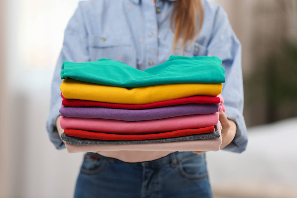 Mulher segurando dobrado roupas limpas dentro de casa, close-up. Dia de lavandaria
 - Foto, Imagem