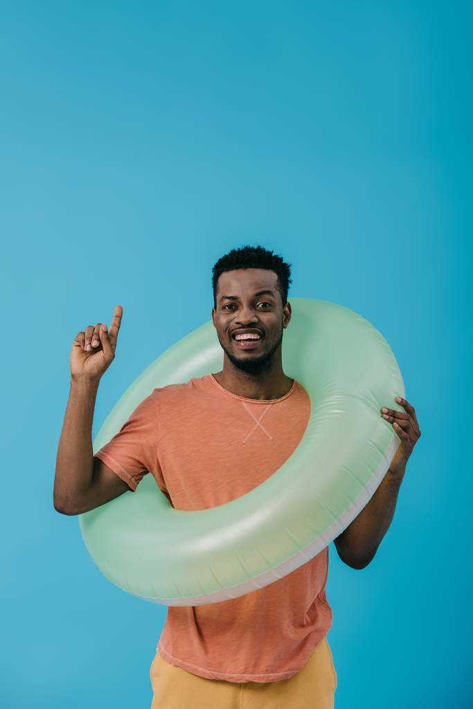 homem americano africano feliz que aponta com o dedo e que está com anel inflável isolado no azul
  - Foto, Imagem