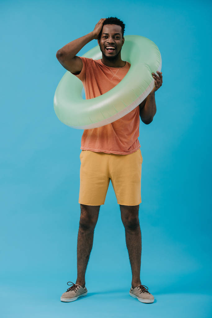 счастливый африканский американец, стоящий с надувным кольцом и трогательными волосами на голубом
  - Фото, изображение