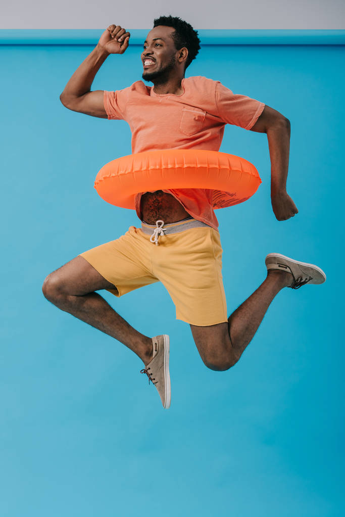 joyeux homme barbu afro-américain sautant avec anneau de natation sur bleu
  - Photo, image