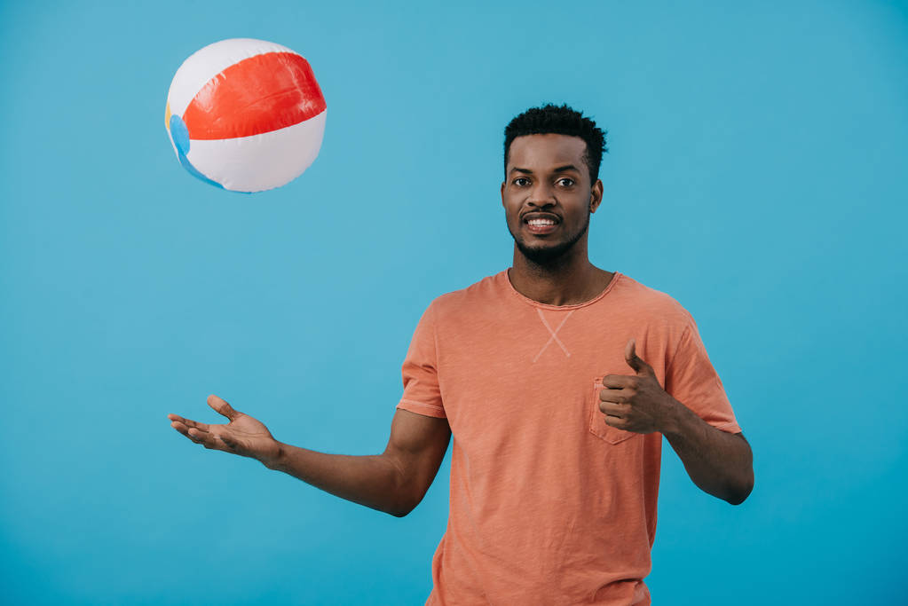 Веселый африканский американец бросает пляжный мяч в воздух, изолированный на голубом
  - Фото, изображение