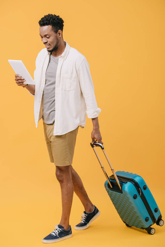 iloinen afrikkalainen amerikkalainen mies tilalla digitaalinen tabletti ja kävely matkatavarat oranssi
 - Valokuva, kuva