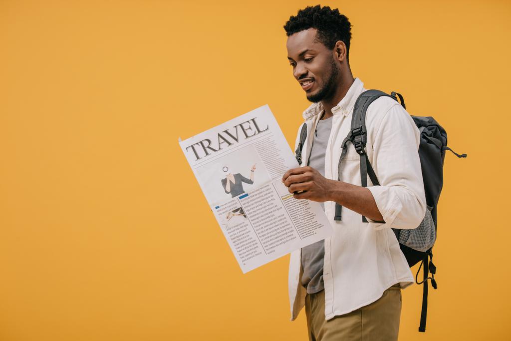веселый африканский американец, стоящий с рюкзаком и читающий туристическую газету, изолированную от апельсина
 - Фото, изображение