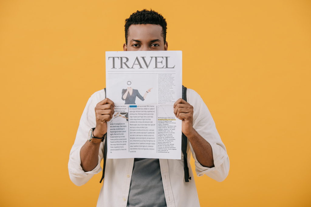 curly african american man covering face with travel newspaper isolated on orange - Photo, Image