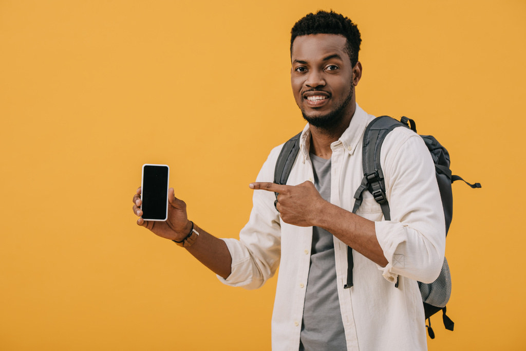 fröhliche afrikanisch-amerikanische Mann zeigt mit dem Finger auf Smartphone mit leerem Bildschirm isoliert auf orange  - Foto, Bild