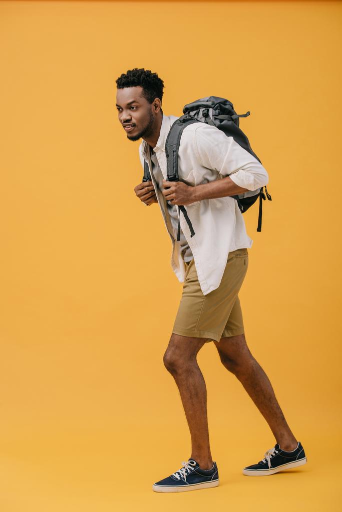 curly happy african american man walking with backpack on orange  - Photo, Image