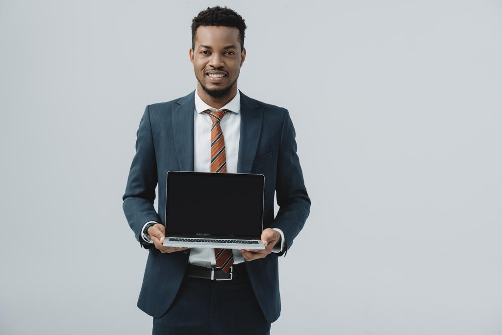 alegre afroamericano hombre sosteniendo portátil con pantalla en blanco aislado en gris
  - Foto, Imagen