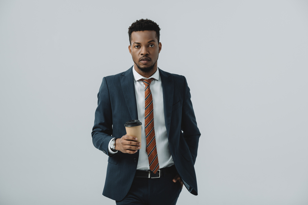 bel homme d'affaires afro-américain tenant la main dans la poche et tenant tasse en papier isolé sur gris
  - Photo, image