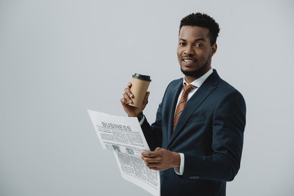 ビジネス新聞と紙コップを灰色で隔離した幸せなアフリカ系アメリカ人男性  - 写真・画像