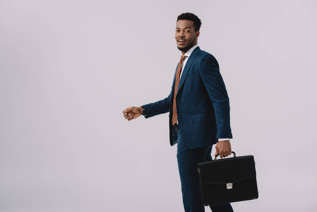 happy african american man in suit holding briefcase isolated on grey  - Photo, Image