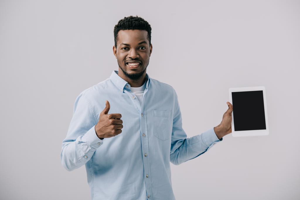 灰色で隔離された空白の画面で親指を表示し、デジタルタブレットを保持する幸せなアフリカ系アメリカ人の男性  - 写真・画像