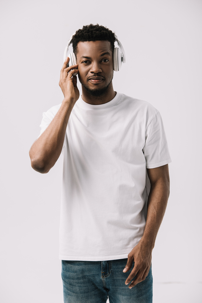 όμορφος Αφρικανός Αμερικανός άνθρωπος ακούγοντας μουσική και αγγίζοντας τα ακουστικά απομονώνονται σε λευκό  - Φωτογραφία, εικόνα