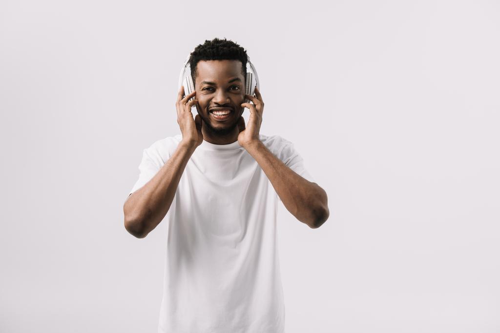 heureux afro-américain homme souriant et touchant écouteurs isolés sur blanc
  - Photo, image