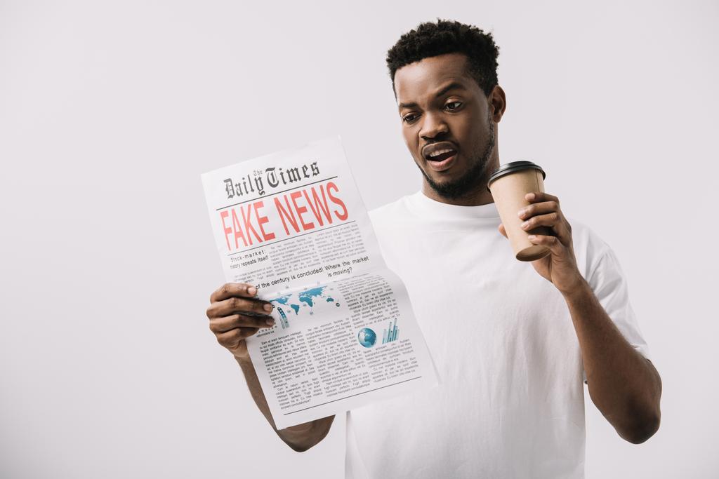 surprised african american man holding paper cup and reading newspaper with fake news lettering isolated on white  - Photo, Image