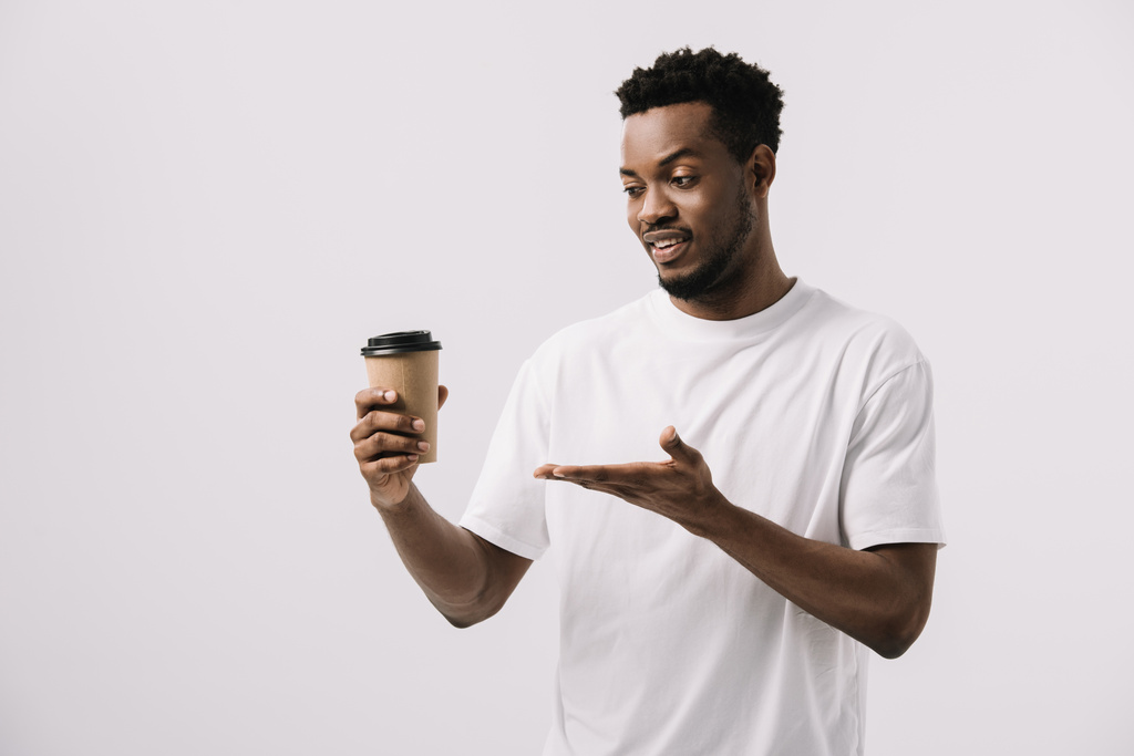 felice uomo africano americano in possesso di tazza di carta e gesticolando isolato su bianco
  - Foto, immagini