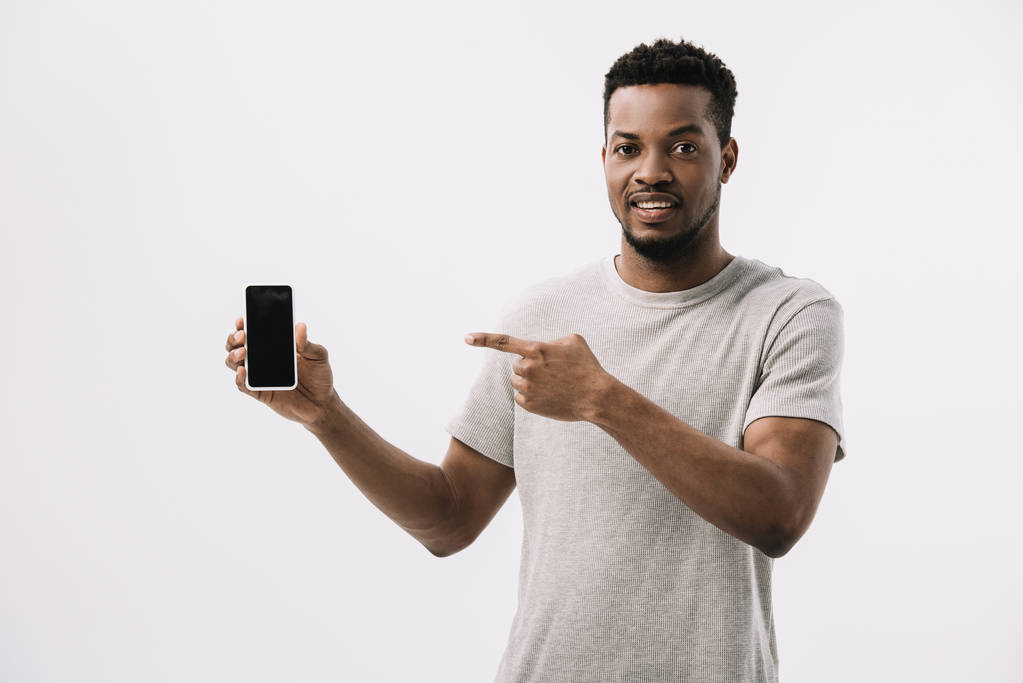 щасливий афроамериканський чоловік вказує пальцем на смартфон з порожнім екраном ізольовано на білому
  - Фото, зображення