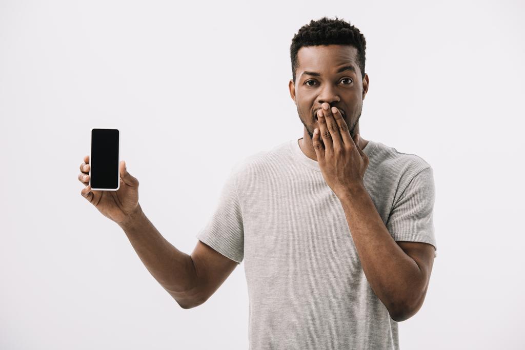 sorprendido hombre afroamericano que cubre la cara y la celebración de teléfono inteligente con pantalla en blanco aislado en blanco
  - Foto, imagen