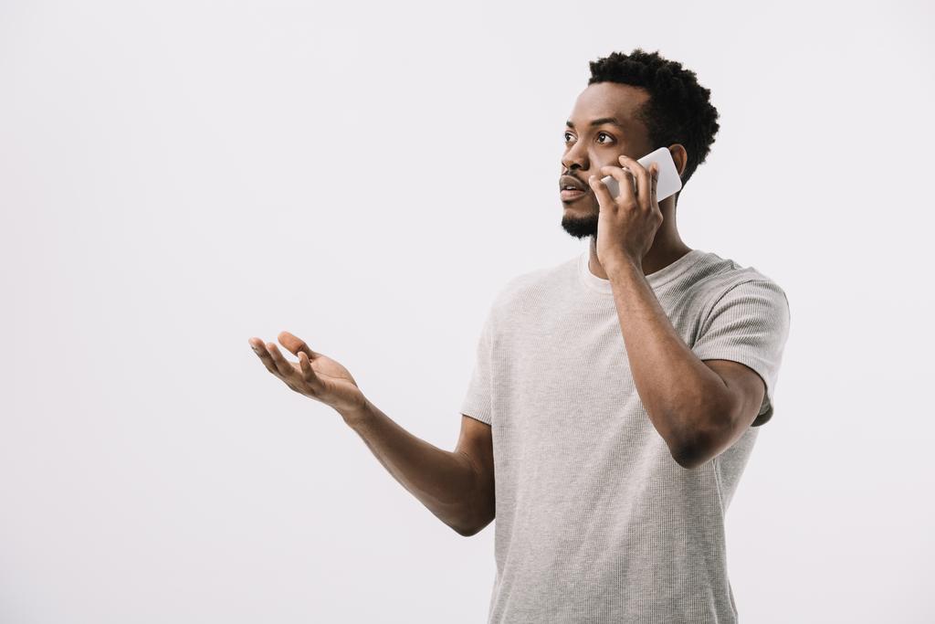 confuso homem afro-americano gesticulando enquanto falava no smartphone isolado no branco
  - Foto, Imagem