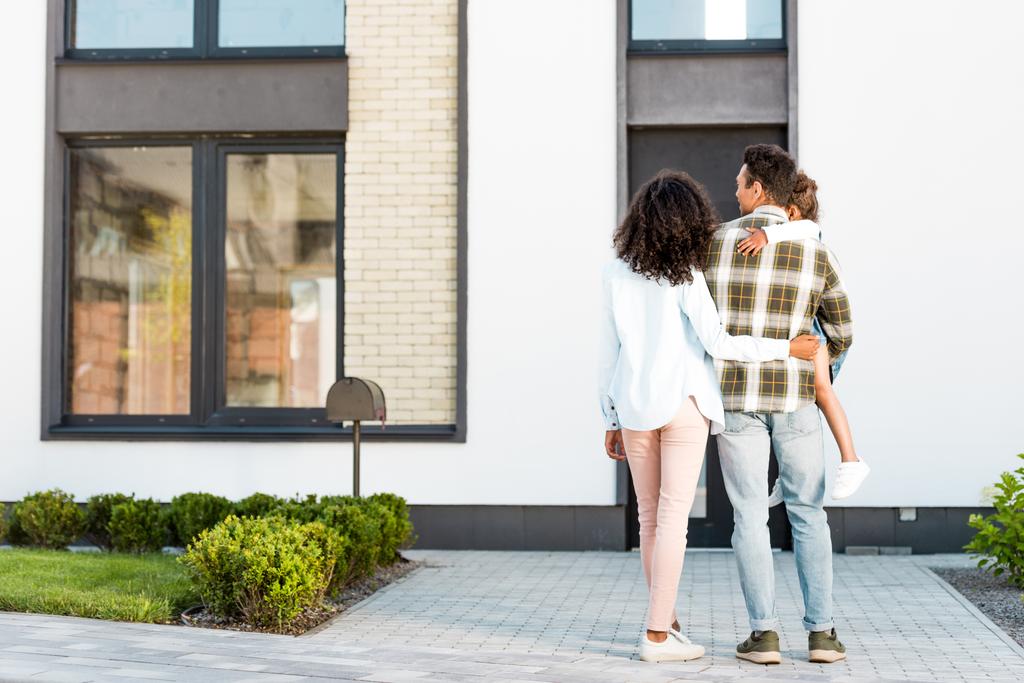vue pleine longueur de la famille afro-américaine debout près de la nouvelle maison tandis que le père tenant enfant et mère étreignant homme
 - Photo, image