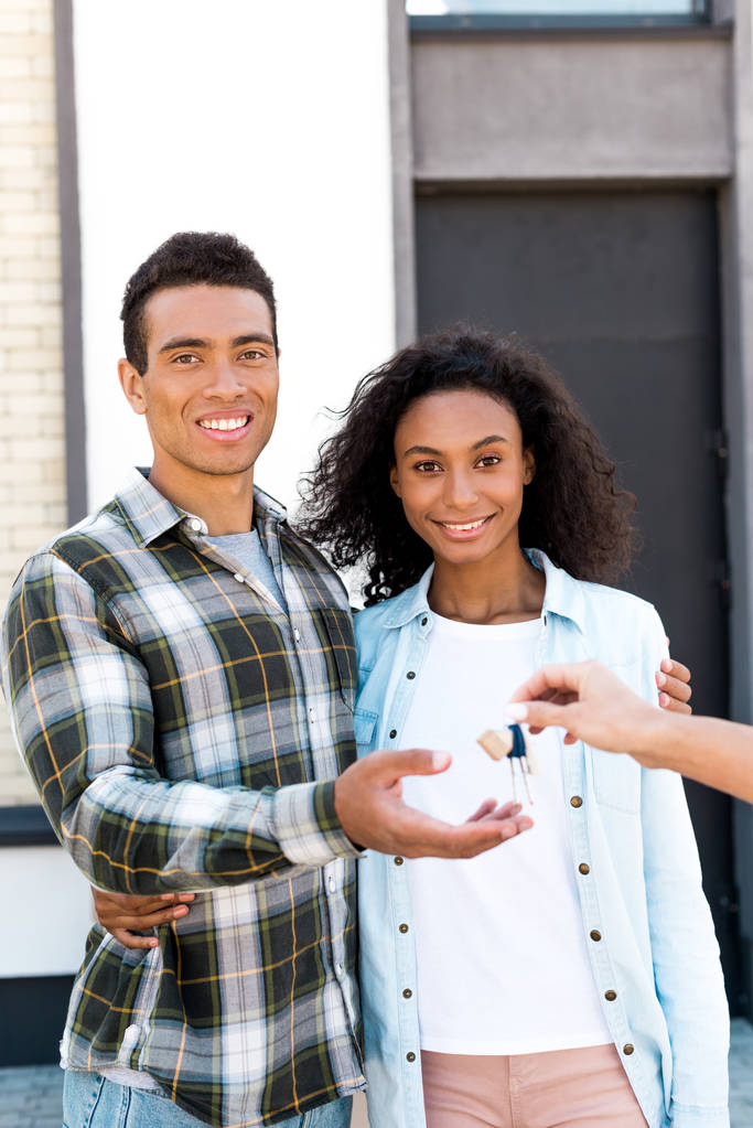 Afrikaans Amerikaans paar kijkt naar camera en glimlachend terwijl je de sleutel van het nieuwe huis neemt - Foto, afbeelding