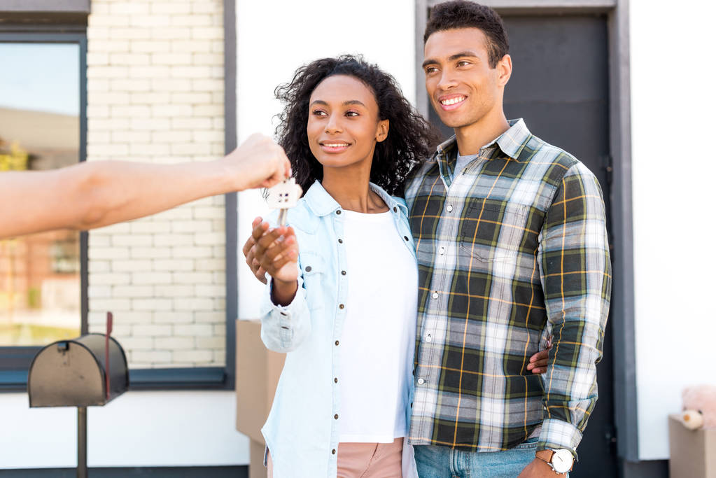pareja afroamericana mirando a la mujer y sonriendo mientras toma la llave de la nueva casa
 - Foto, Imagen