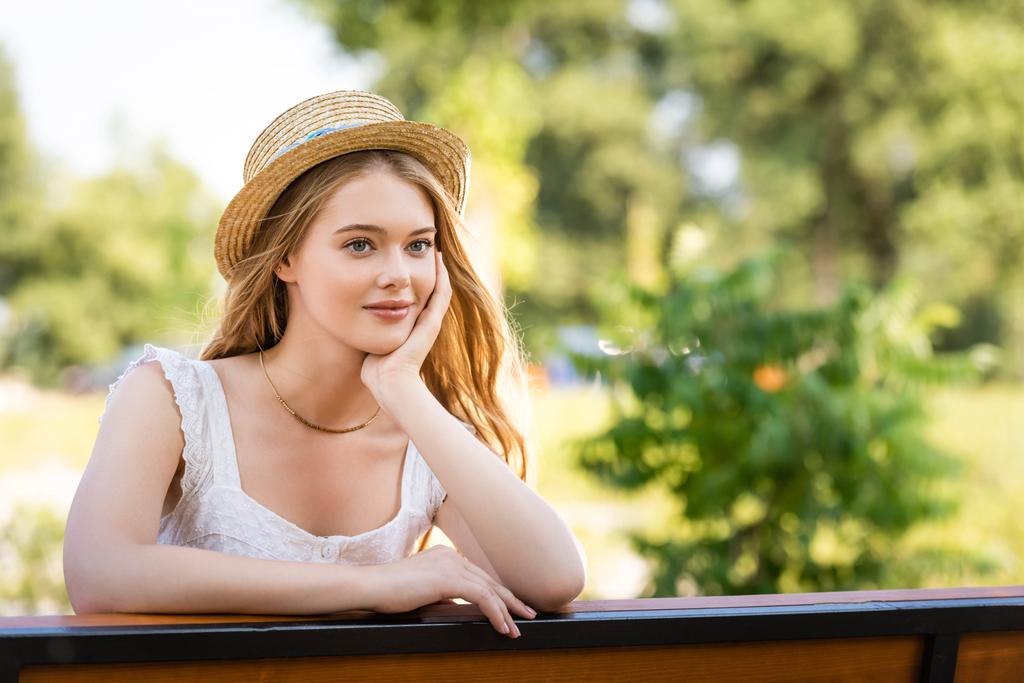  bella ragazza in cappello di paglia in posa mentre seduto sulla panchina e guardando altrove
 - Foto, immagini