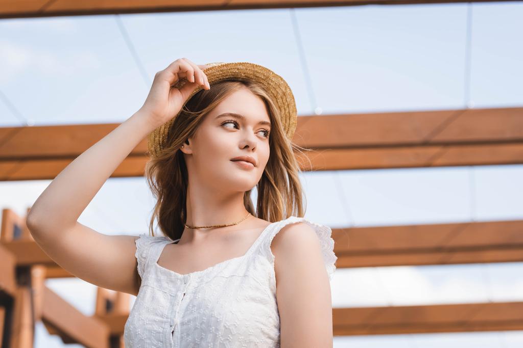 Низкий угол зрения красивой девушки в соломенной шляпе, отводящей взгляд
 - Фото, изображение