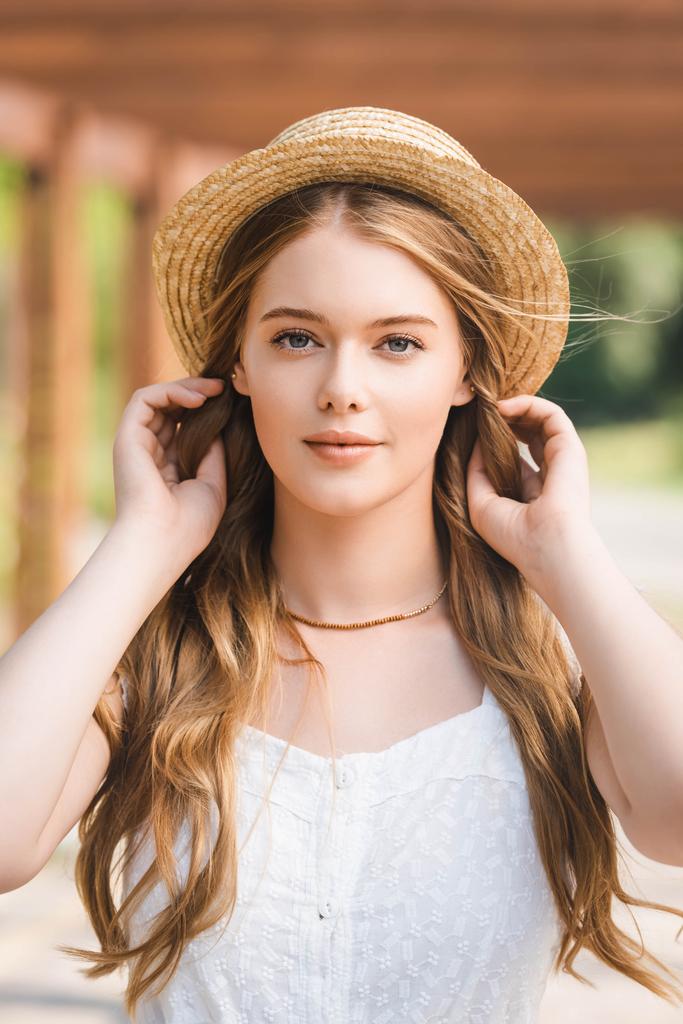 portrait shot of beautiful girl in straw hat touching hair while looking at camera - Photo, Image
