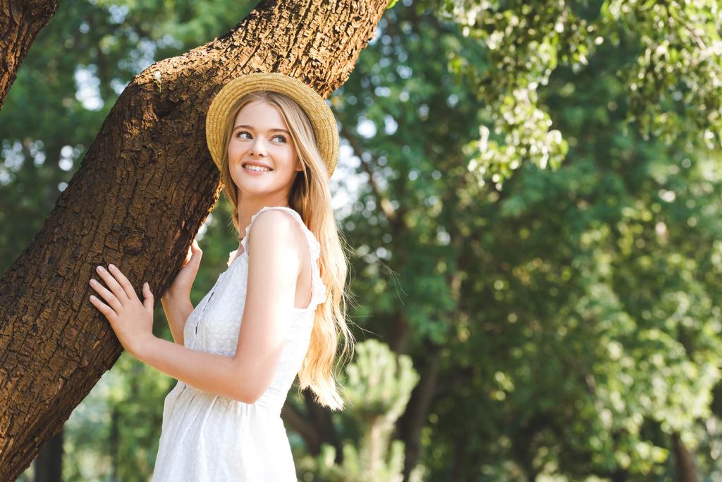 belle jeune fille en robe blanche et chapeau de paille debout près du tronc d'arbre
 - Photo, image