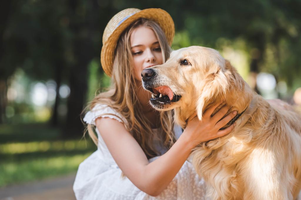  menina bonita em vestido branco e palha petting golden retriever e olhando para o cão
 - Foto, Imagem