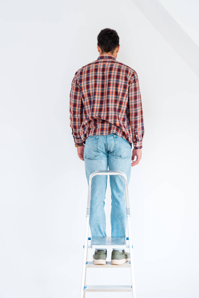 Rückansicht eines Mannes, der an der Leiter steht und isoliert auf weiße Wand blickt - Foto, Bild