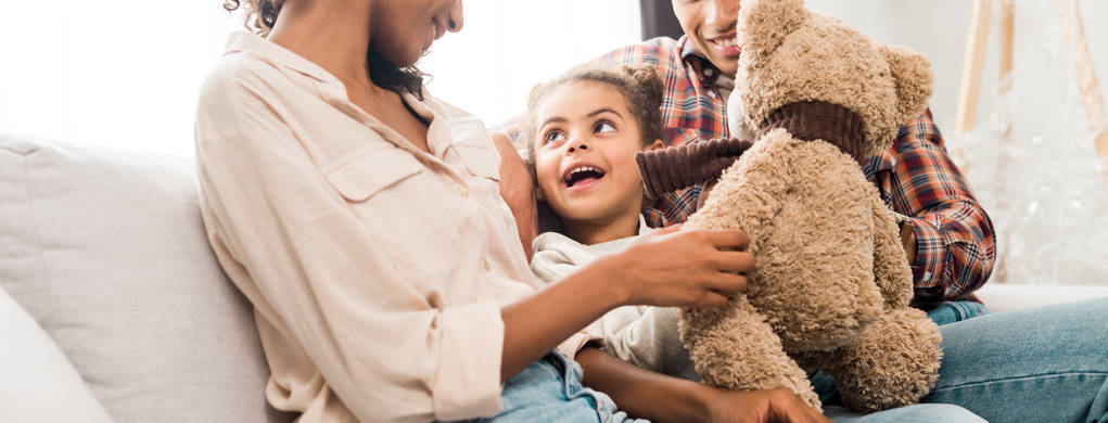 panoramatický záběr afroamerické rodiny sedící na pohovce, zatímco dítě drží medvídka a dívá se na matku   - Fotografie, Obrázek