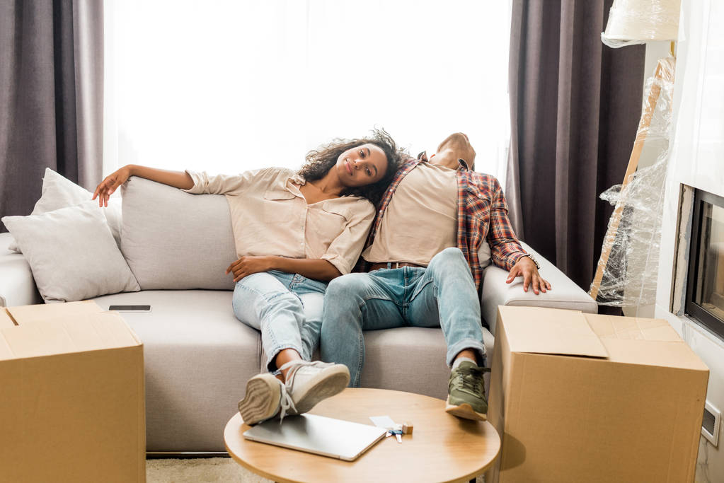 vista completa de la longitud de marido durmiendo en el sofá, mientras que la esposa sentado cerca del hombre y mirando a la cámara
  - Foto, imagen