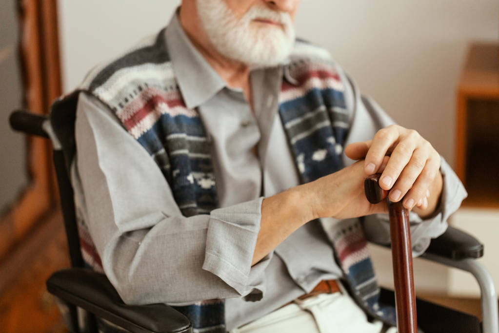 Homem idoso sozinho sentado na cadeira de rodas e segurando uma bengala
 - Foto, Imagem