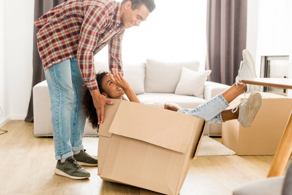 vista de longitud completa de hombre y mujer afroamericanos mirándose mientras marido tratando de mover caja con esposa
 - Foto, imagen