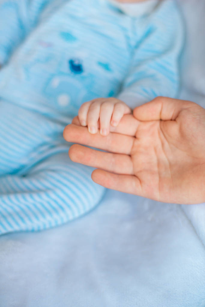 A mão da mãe segura um bebezinho bonito em sua mão em casa na cama. Mãe feliz
 - Foto, Imagem