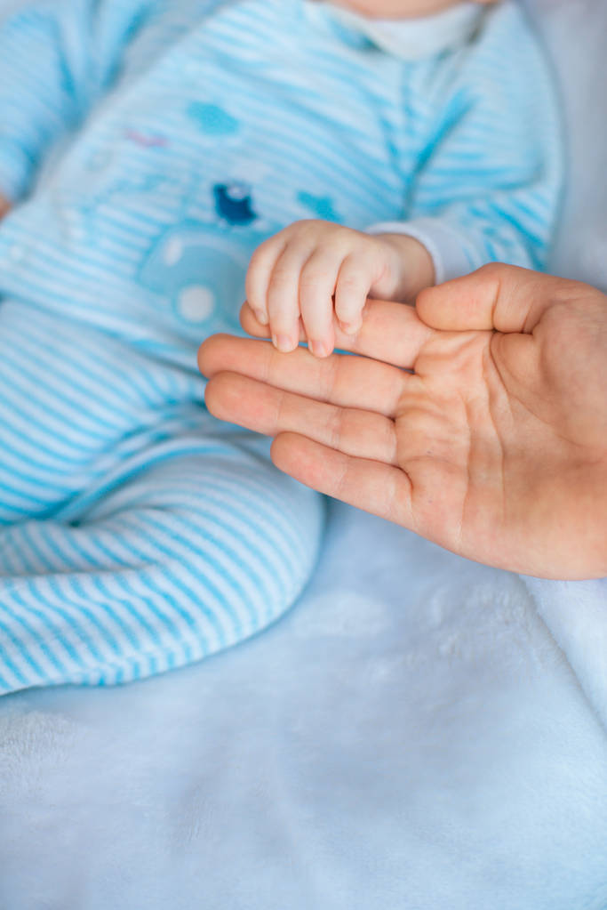 Ręka matki trzyma cute małego dziecka w ręku w domu na łóżku. Szczęśliwa macierzyństwo - Zdjęcie, obraz