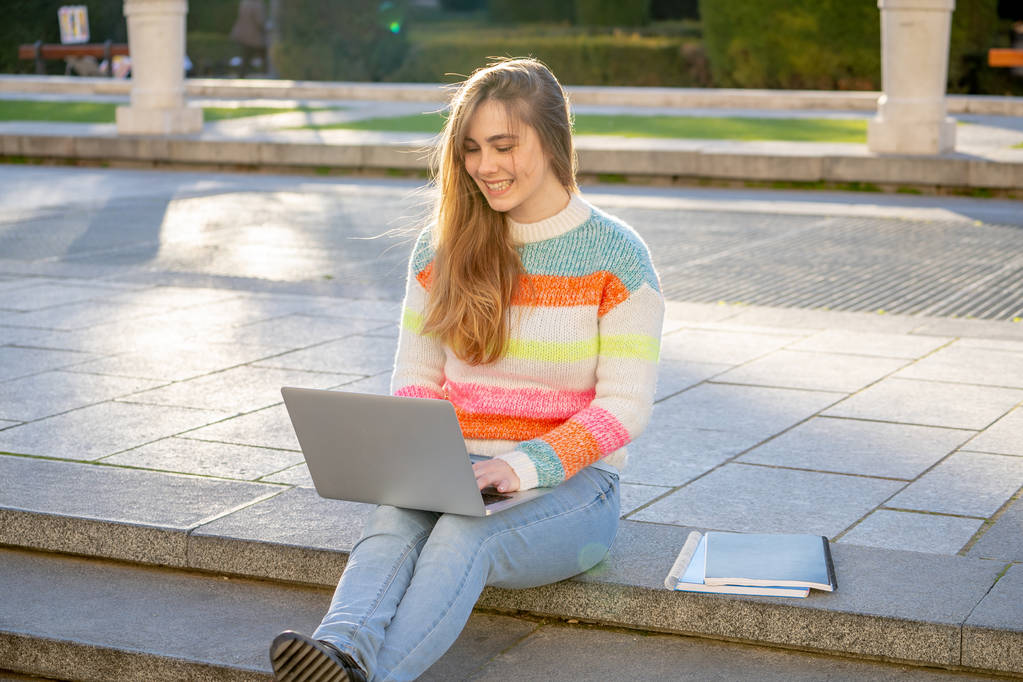 Elég fiatal vidám tinédzser nő dolgozik vagy tanul a laptop számítógép ül boldog és a lépcsőn a város szabadtéri városi háttérben. A hallgatói életmód online oktatás és technológia koncepció. - Fotó, kép