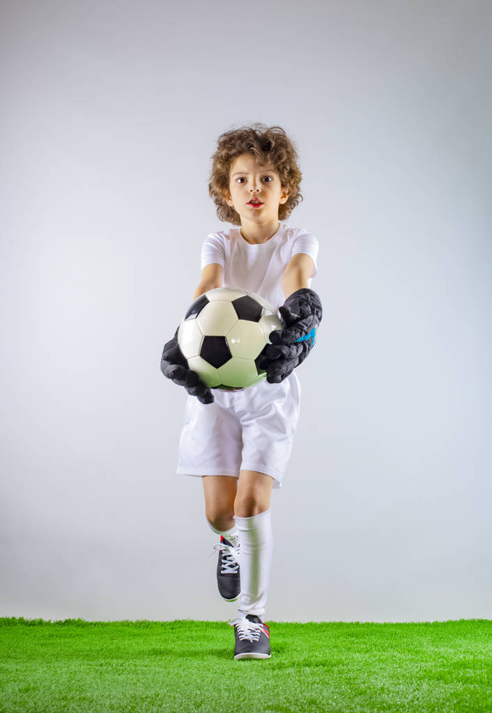 Kid-foci bajnok. Fiú kapus a futball sportruházat a labdát, szürke háttér. Sportkoncepció. Lemezterület másolása. - Fotó, kép